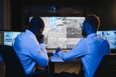 İki erkek güvenlik görevlisi bilgisayar ekranına bakarken biri videonun detaylarını anlatıyor..