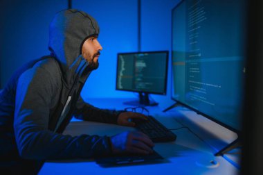 Bilgisayar programcısı karanlık odada bilgisayar kullanıyor.