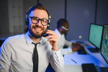 Mutlu Güvenilir Teknik Müşteri Destek Uzmanı Meslektaşlar ve Ekranlarla Dolu Gözetleme ve Kontrol Odasında Kulaklık Çağrısı Yapıyor.