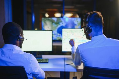 Mutlu Güvenilir Teknik Müşteri Destek Uzmanı Meslektaşlar ve Ekranlarla Dolu Gözetleme ve Kontrol Odasında Kulaklık Çağrısı Yapıyor.