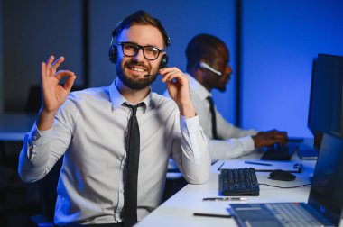 Erkek Veri Bilimadamı, Büyük Altyapı Kontrol ve İzleme Odası 'nda Kulaklık Takan Kişisel Bilgisayarda Çalışıyor. İş Çağrı Merkezi Ofisi 'nde Genç Mühendis