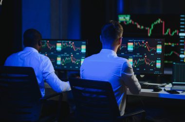 İki işadamı, finans analisti ya da yatırım danışmanı ellerinde polis bilgisayarları ve belgelerle büro masasında oturuyorlar.