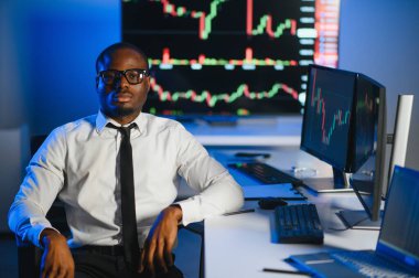 Afro-amerikan borsa bürosunda çalışan borsacı veya komisyoncu. Arka planda veri, saat numaraları ve grafikleri gösteren monitörlerin bilgisayarını kullanıyor..