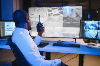 Afro-Amerikan güvenlik operatörünün arka görüntüsü. Güvenlik kamerası görüntülerini gösteren ekranları olan bir bilgisayar kullanın. .