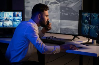 CCTV görüntülerine bakarken telsiz kullanan güvenlik sistemi operatörünün yan görüntüsü.