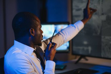 Afro-Amerikan güvenlik operatörünün arka görüntüsü. Güvenlik kamerası görüntülerini gösteren ekranları olan bir bilgisayar kullanın. .