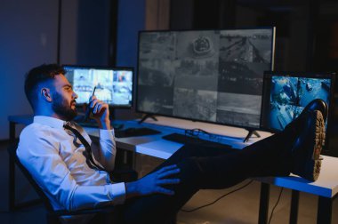 Erkek güvenlik görevlisi, bilgisayardaki birden fazla CCTV görüntüsünü izlerken telsizden konuşuyor..