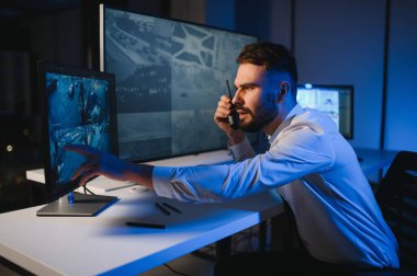 CCTV görüntülerine bakarken telsiz kullanan güvenlik sistemi operatörünün yan görüntüsü.