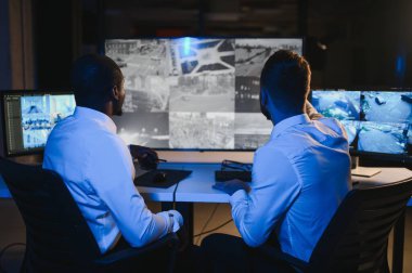 İki erkek güvenlik görevlisi bilgisayar ekranına bakarken biri videonun detaylarını anlatıyor..