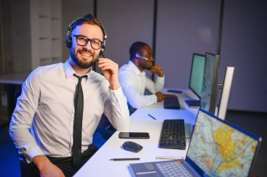 Mutlu Güvenilir Teknik Müşteri Destek Uzmanı Meslektaşlar ve Ekranlarla Dolu Gözetleme ve Kontrol Odasında Kulaklık Çağrısı Yapıyor.