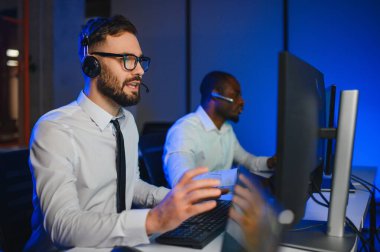 Erkek Veri Bilimadamı, Büyük Altyapı Kontrol ve İzleme Odası 'nda Kulaklık Takan Kişisel Bilgisayarda Çalışıyor. İş Çağrı Merkezi Ofisi 'nde Genç Mühendis