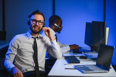 Çağrı merkezinde eller ücretsiz kulaklık kullanırken müşteriye bir şey açıklamaya çalışan erkek teknik destek ajanı.