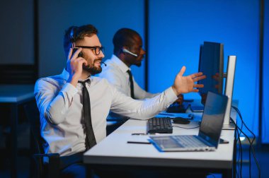 Erkek Veri Bilimadamı, Büyük Altyapı Kontrol ve İzleme Odası 'nda Kulaklık Takan Kişisel Bilgisayarda Çalışıyor. İş Çağrı Merkezi Ofisi 'nde Genç Mühendis