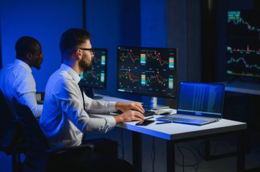 Finansal Analizci İş Gecesinde Yatırım Bankeriyle Konuşuyor. Çoklu Monitör Çalışma İstasyonunda Gerçek Zaman Stok Çizelgesi Verisi Hakkında Sohbet