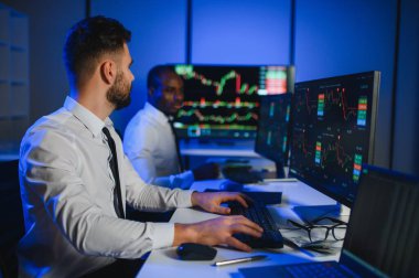 İki işadamı, finans analisti ya da yatırım danışmanı ellerinde polis bilgisayarları ve belgelerle büro masasında oturuyorlar.