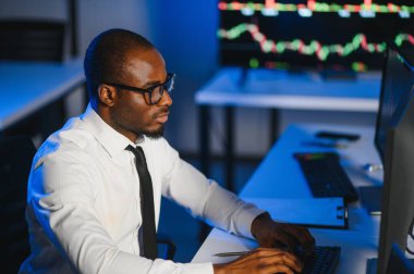 Gerçek zamanlı hisse senetleri, emtialar ve borsa grafikleri ile birlikte Multi-Monitor Workstation ile bilgisayar üzerinde çalışan finansal analist. Afrikalı Amerikalı İşadamı Gece Yatırım Bankası 'nda çalışıyor.