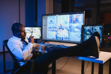 Afro-Amerikan güvenlik görevlisi ya da merkez bilgisayar ve telsiz kullanıyor, ekranlara bakıyor..