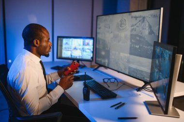 Ciddi bir Afrikalı Amerikalı güvenlik görevlisi güvenlik odasında güvenlik kamerası görüntülerini izlerken bilgisayar ekranından otel hayatını izliyor.