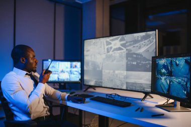 Afro-Amerikalı güvenlik görevlisi kontrol odasında telsizle konuşuyor..