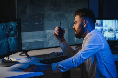 CCTV görüntülerine bakarken telsiz kullanan güvenlik sistemi operatörünün yan görüntüsü.