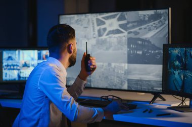 CCTV görüntülerine bakarken telsiz kullanan güvenlik sistemi operatörünün yan görüntüsü.