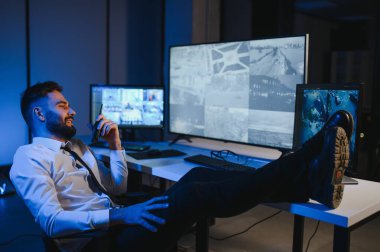 CCTV görüntülerine bakarken telsiz kullanan güvenlik sistemi operatörünün yan görüntüsü.