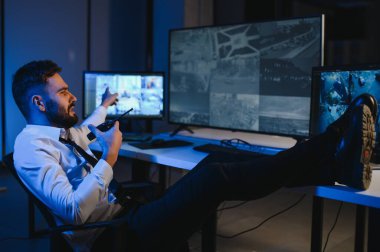 Erkek güvenlik görevlisi, bilgisayardaki birden fazla CCTV görüntüsünü izlerken telsizden konuşuyor..