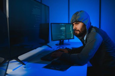 Bilgisayarlı bir hacker, kapüşonlu bir masada oturan bir adam..