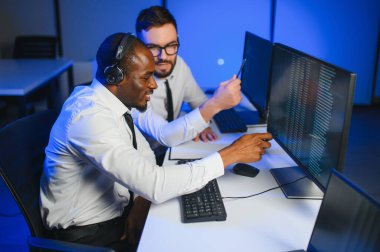 Mutlu Güvenilir Teknik Müşteri Destek Uzmanı Meslektaşlar ve Ekranlarla Dolu Gözetleme ve Kontrol Odasında Kulaklık Çağrısı Yapıyor.