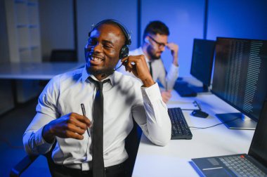 Erkek Veri Bilimadamı, Büyük Altyapı Kontrol ve İzleme Odası 'nda Kulaklık Takan Kişisel Bilgisayarda Çalışıyor. İş Çağrı Merkezi Ofisi 'nde Genç Mühendis