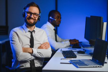 Çağrı merkezinde eller ücretsiz kulaklık kullanırken müşteriye bir şey açıklamaya çalışan erkek teknik destek ajanı.