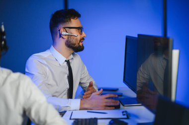 Erkek Veri Bilimadamı, Büyük Altyapı Kontrol ve İzleme Odası 'nda Kulaklık Takan Kişisel Bilgisayarda Çalışıyor. İş Çağrı Merkezi Ofisi 'nde Genç Mühendis