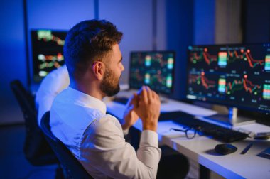 İki işadamı, finans analisti ya da yatırım danışmanı ellerinde polis bilgisayarları ve belgelerle büro masasında oturuyorlar.