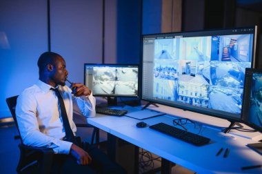 Afro-Amerikan güvenlik görevlisi ya da merkez bilgisayar ve telsiz kullanıyor, ekranlara bakıyor..