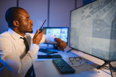 Afro-Amerikalı güvenlik görevlisi kontrol odasında telsizle konuşuyor..