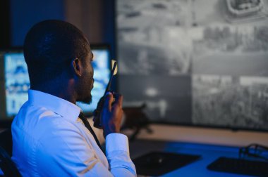 Afro-Amerikan güvenlik görevlisi ya da merkez bilgisayar ve telsiz kullanıyor, ekranlara bakıyor..