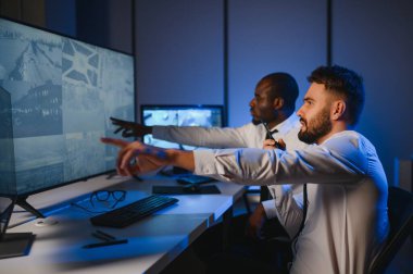 Güvenlik Kontrol Odası İki Subay Şüpheli Faaliyetler İçin Çoklu Ekranları İzlerken Telsiz ile İzinsiz Faaliyetler Raporluyorlar. Ulusal Önemliliğin İtirazını Korurlar.