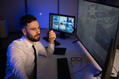 Erkek güvenlik görevlisi, bilgisayardaki birden fazla CCTV görüntüsünü izlerken telsizden konuşuyor..