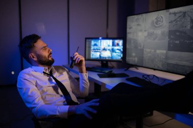 CCTV görüntülerine bakarken telsiz kullanan güvenlik sistemi operatörünün yan görüntüsü.