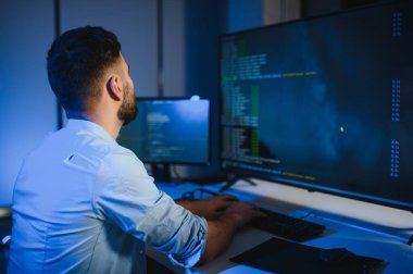 Bilgisayarda çalışan bilişim programcısı. Erkek Uzman Yaratıcı Yenilikçi Yazılım Mühendisliği Geliştirme Uygulaması, Program, Video Oyunu. Kodlama Dili Terminali. Omuz üstünden.