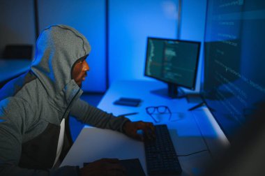 Bilgisayar programcısı karanlık odada bilgisayar kullanıyor.