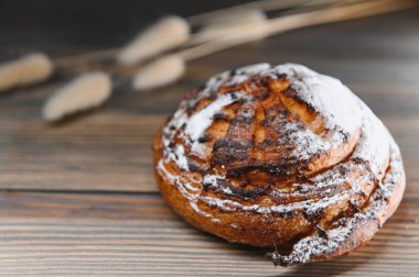 Tatlı tarçınlı çörek, ahşap bir arka planda kıvrılıyor..
