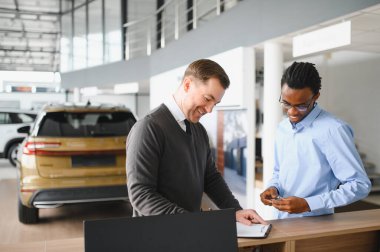 Müşteri erkek, galeride otomobil satın alıyor, araba satıcısıyla kağıt imzalıyor. Galeride yeni otomobil alma kavramı.