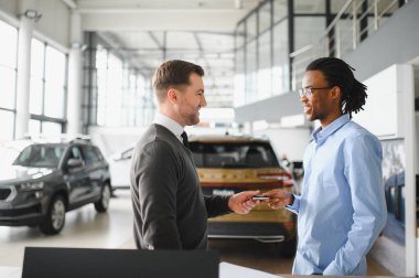 Müşteri erkek, galeride otomobil satın alıyor, araba satıcısıyla kağıt imzalıyor. Galeride yeni otomobil alma kavramı.