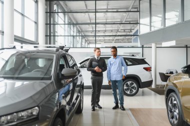 Erkek müşterinin portresi galeride profesyonel araba satıcısıyla konuşuyor. Yeni otomobil seçimi ve satın alma kavramı.