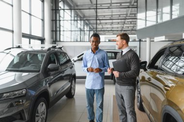 Erkek müşterinin portresi galeride profesyonel araba satıcısıyla konuşuyor. Yeni otomobil seçimi ve satın alma kavramı.