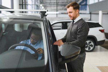 Erkek araba satıcısı, galeride dalgın genç bir müşteriyle sohbet ediyor. Satış merkezinden araba alırken adam dinliyor.