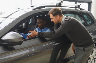 Erkek müşterinin portresi galeride profesyonel araba satıcısıyla konuşuyor. Yeni otomobil seçimi ve satın alma kavramı.