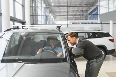 Erkek araba satıcısı, galeride dalgın genç bir müşteriyle sohbet ediyor. Satış merkezinden araba alırken adam dinliyor.