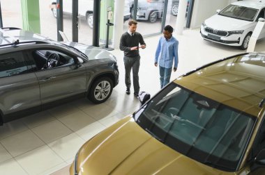 Erkek müşterinin portresi galeride profesyonel araba satıcısıyla konuşuyor. Yeni otomobil seçimi ve satın alma kavramı.